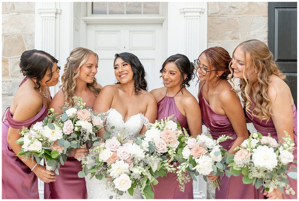 bride surrounded closely by her bridesmaids as they all smile and look at each other at the barn at silverstone