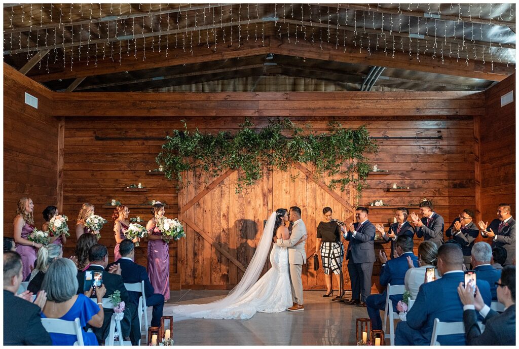 couple sharing their first kiss inside beautiful barn wedding ceremony on summer day at the barn at silverstone