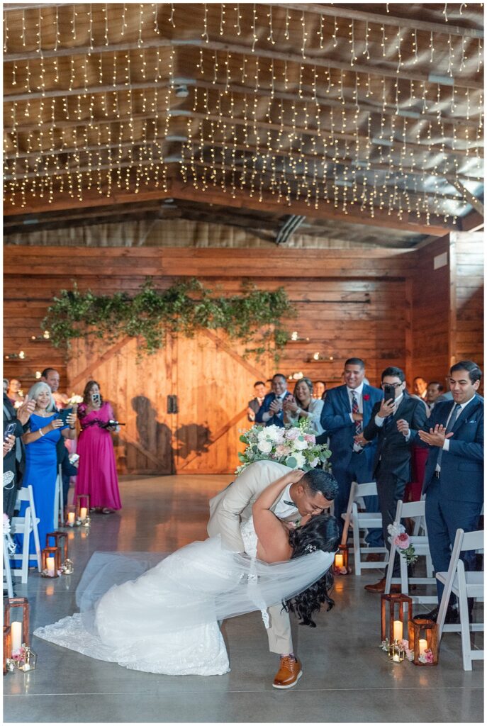 groom dipping his bride way back and kissing her as they exit their wedding ceremony and guests applaud at the barn at silverstone