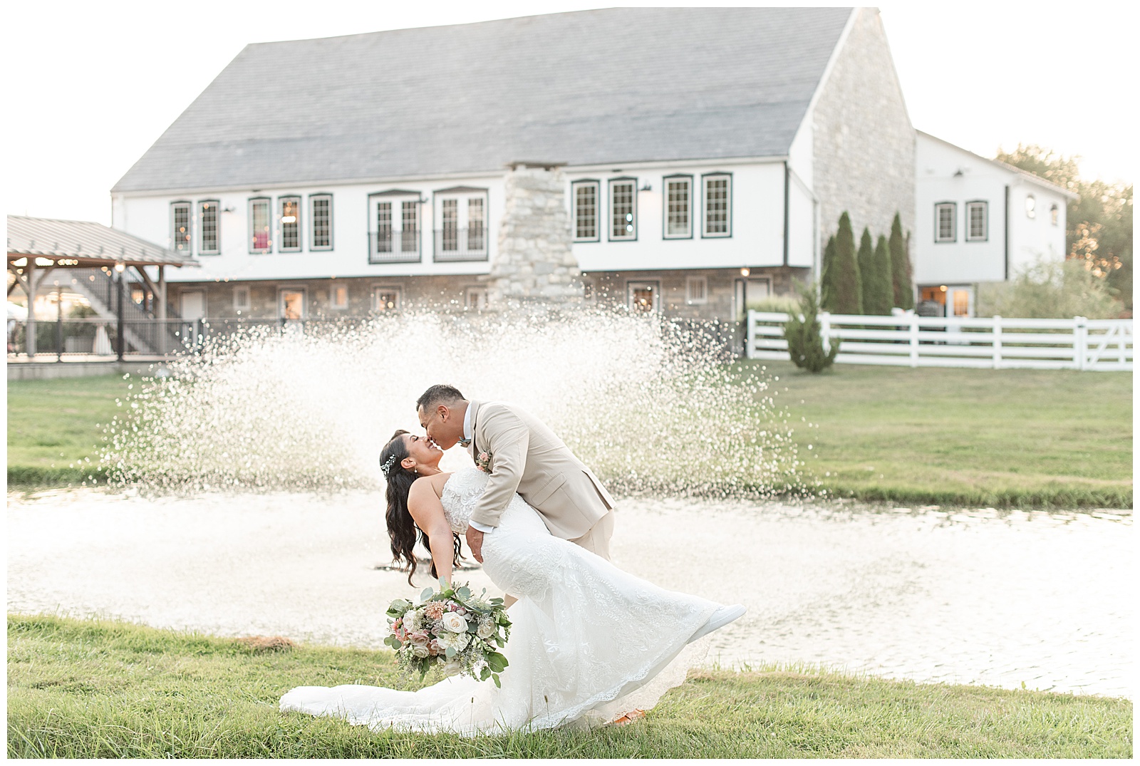 groom dipping his bride back as they kiss by the pond with fountain and barn in background in lancaster county