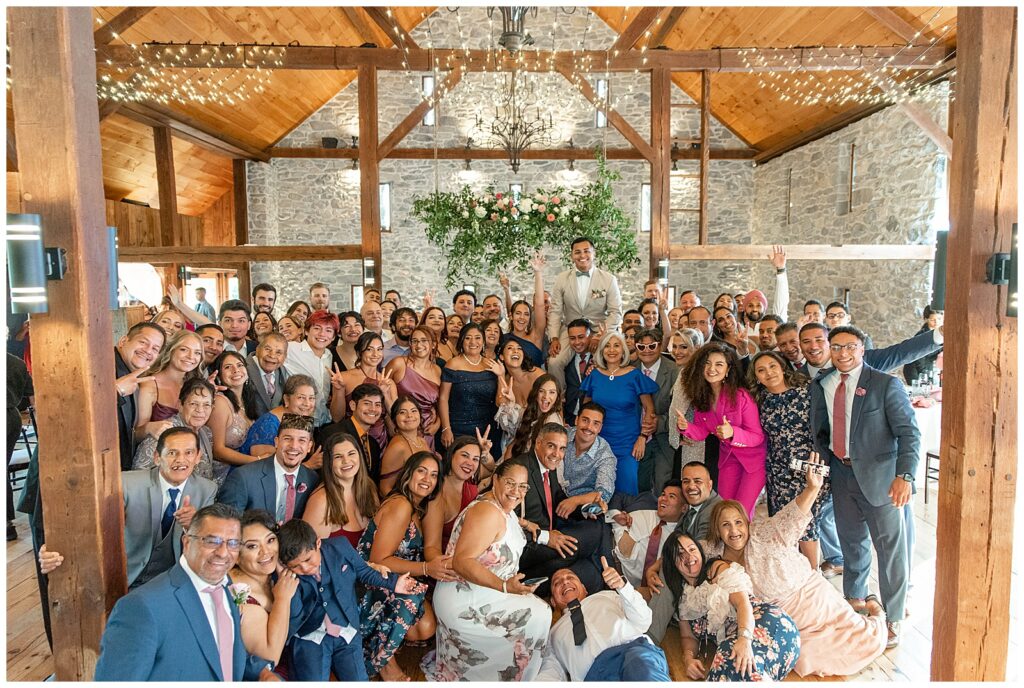couple with all of their guests inside beautiful barn during their reception at the barn at silverstone in lancaster pennsylvania