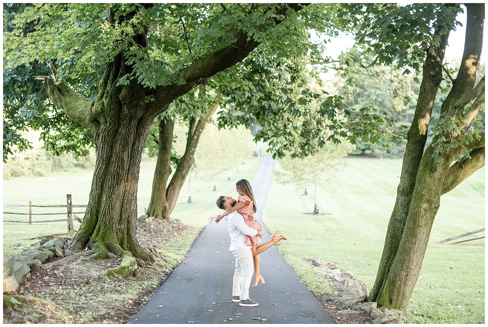 guy lifting up girl as they both look at each other on paved tree-lined path at Domaine Pterion