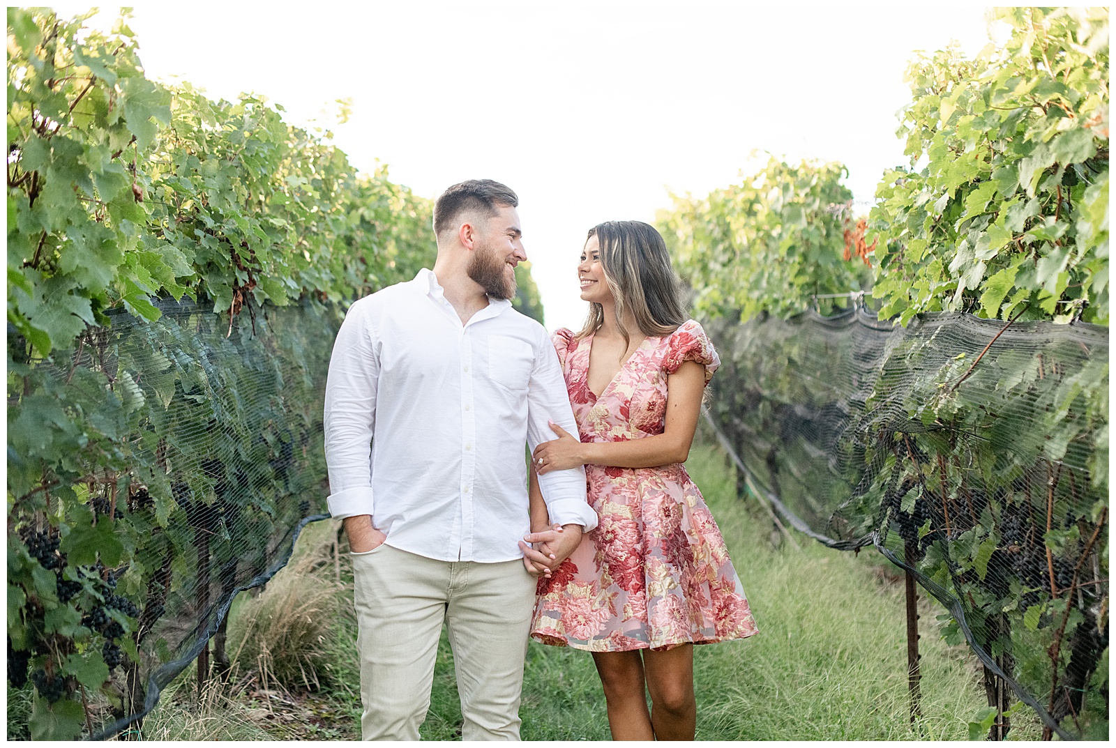 couple standing close as woman holds onto man's left arm in between rows of grape trees at Domaine Pterion vineyard and winery