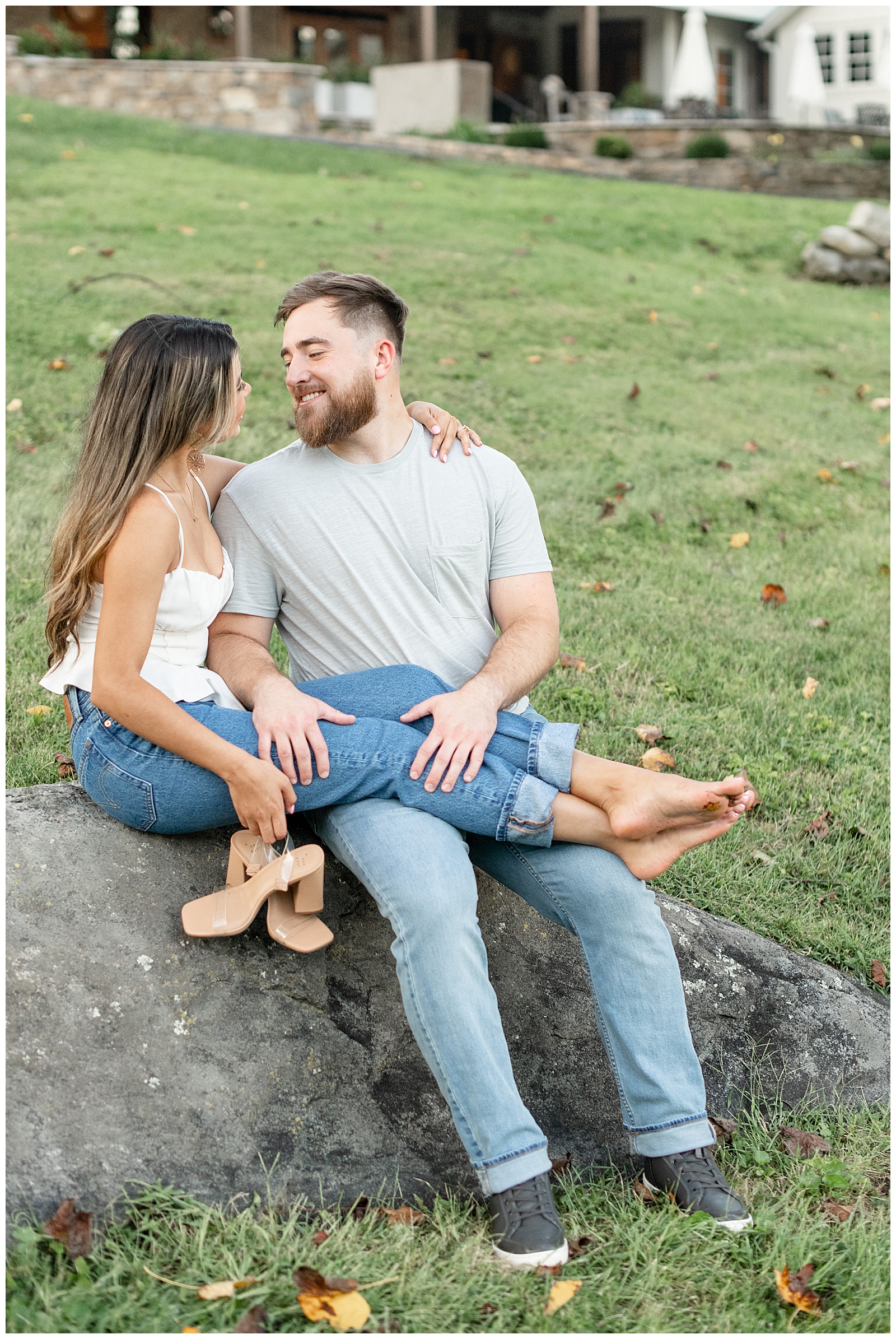 couple sitting on large rock with girl in white tank top and blue jeans draping her legs over guy who's also wearing white shirt and blue jeans at Domaine Pterion