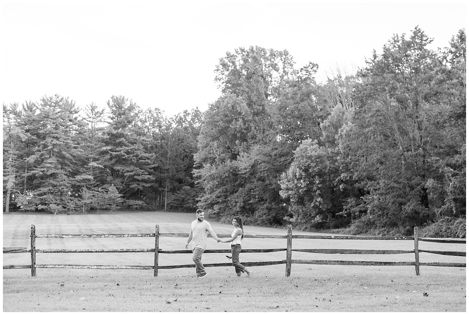 black and white photo of guy holding girl's hand and leading her along wooden fence at Domaine Pterion