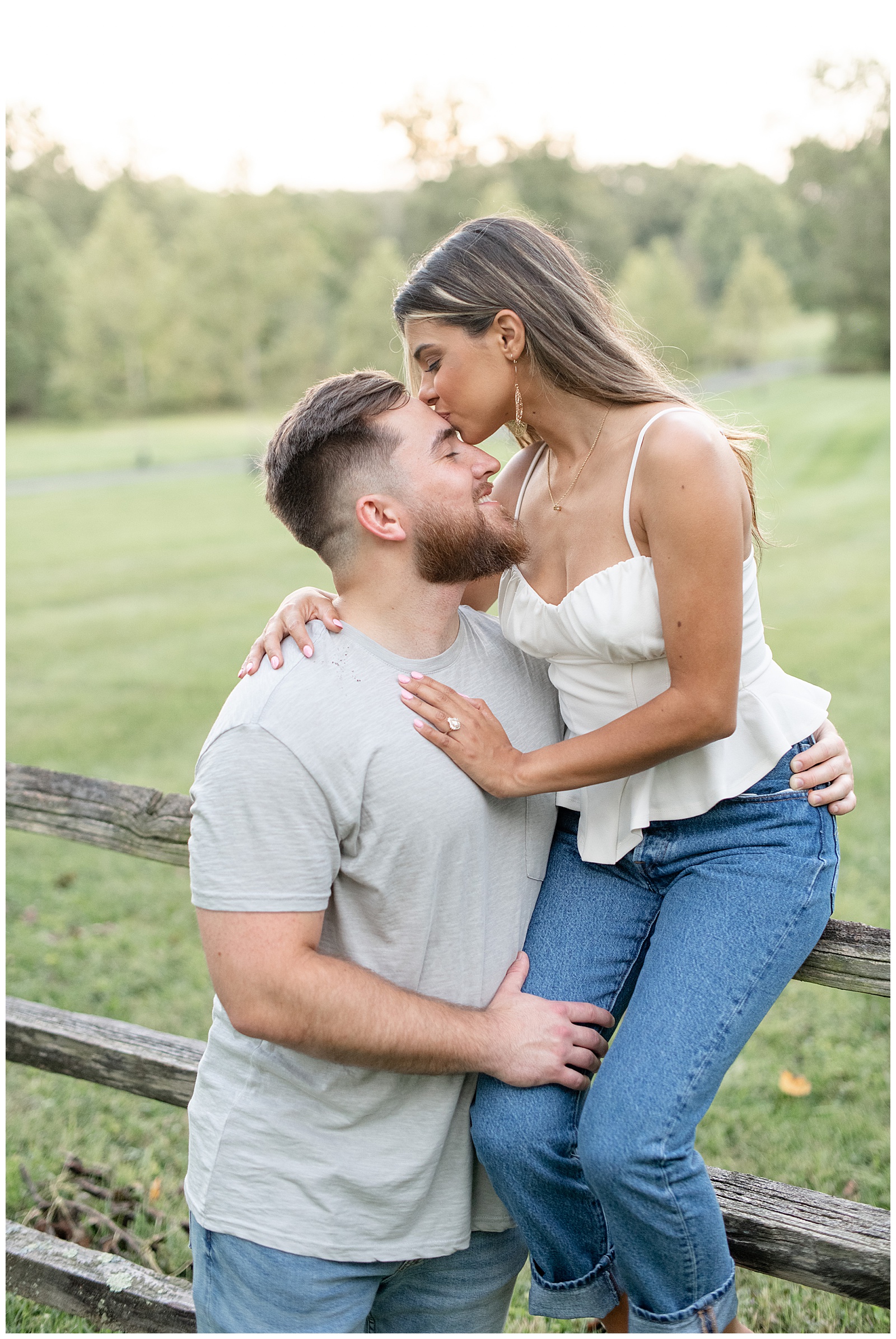 woman sitting on top rail of wooden fence and being supported by her man as she kisses his forehead at Domaine Pterion vineyard and winery