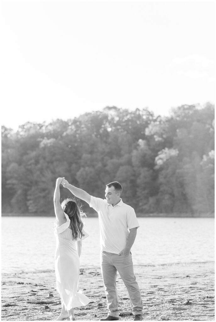 black and white photo of guy twirling girl under his right arm beside water at lake redman