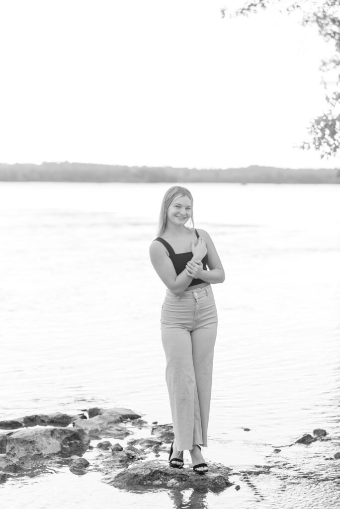 black and white photo of girl standing along shore line with right hand touching left shoulder by susquehanna river in lancaster pa