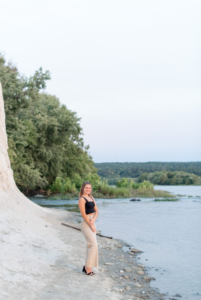 senior girl standing along waters edge at sunset by river in lancaster pennsylvania