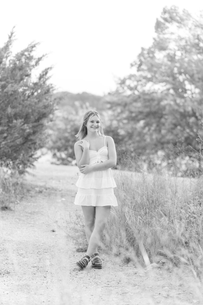 black and white photo of senior girl in white dress standing by wild grasses at white cliffs of conoy in lancaster pa