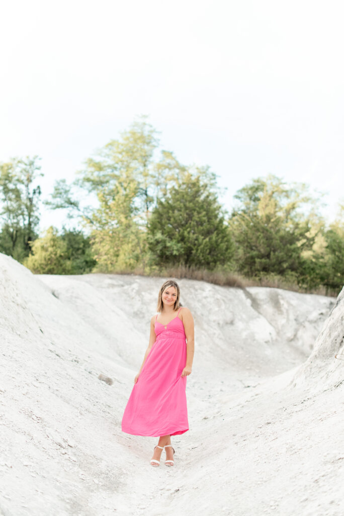 senior girl standing on white rock holding sides of her long dress at sunset at white cliffs of conoy