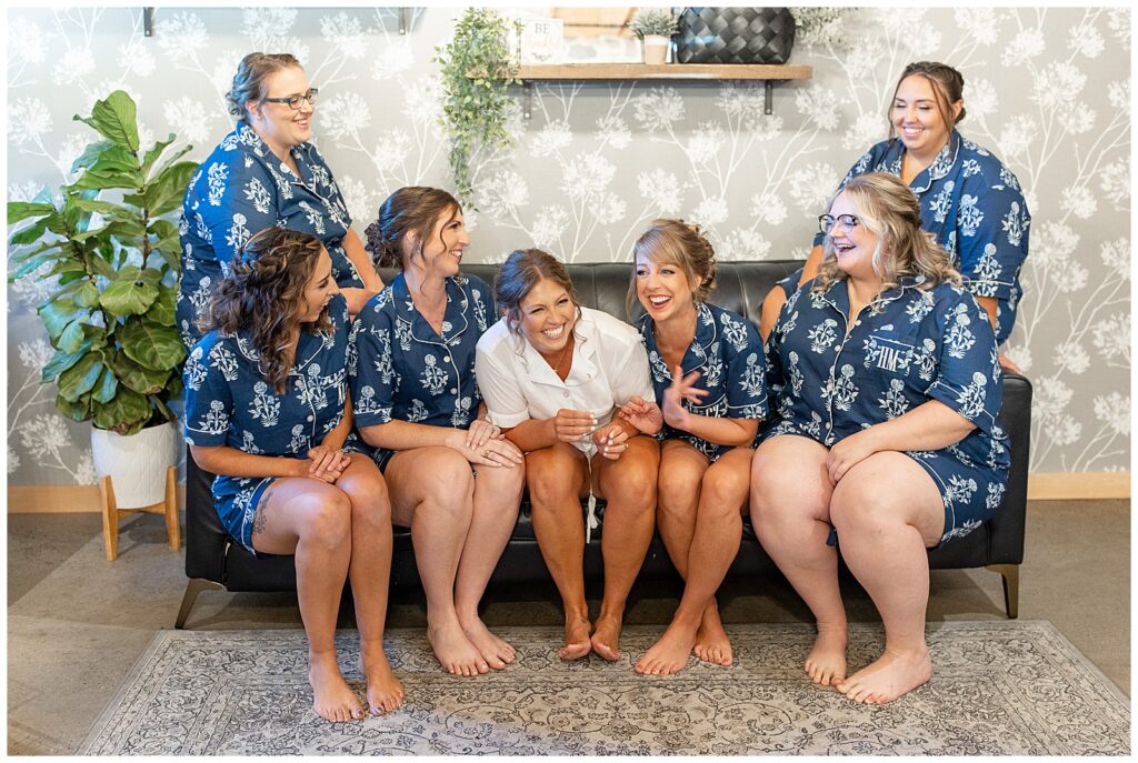 bride and bridesmaids all in robes sitting on chair and laughing in bridal suite at brick gables