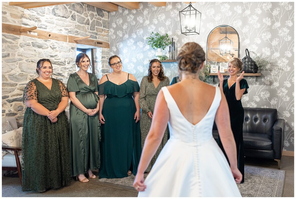 back of bride towards camera as she shares first look moment with her bridesmaids in bridal suite at brick gables