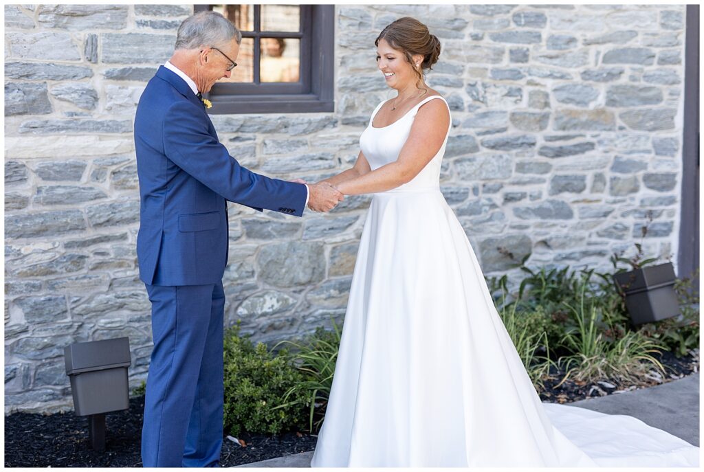 bride sharing first look moment with her dad who's wearing a blue suit outside stone building at brick gables in lititz pennsylvania