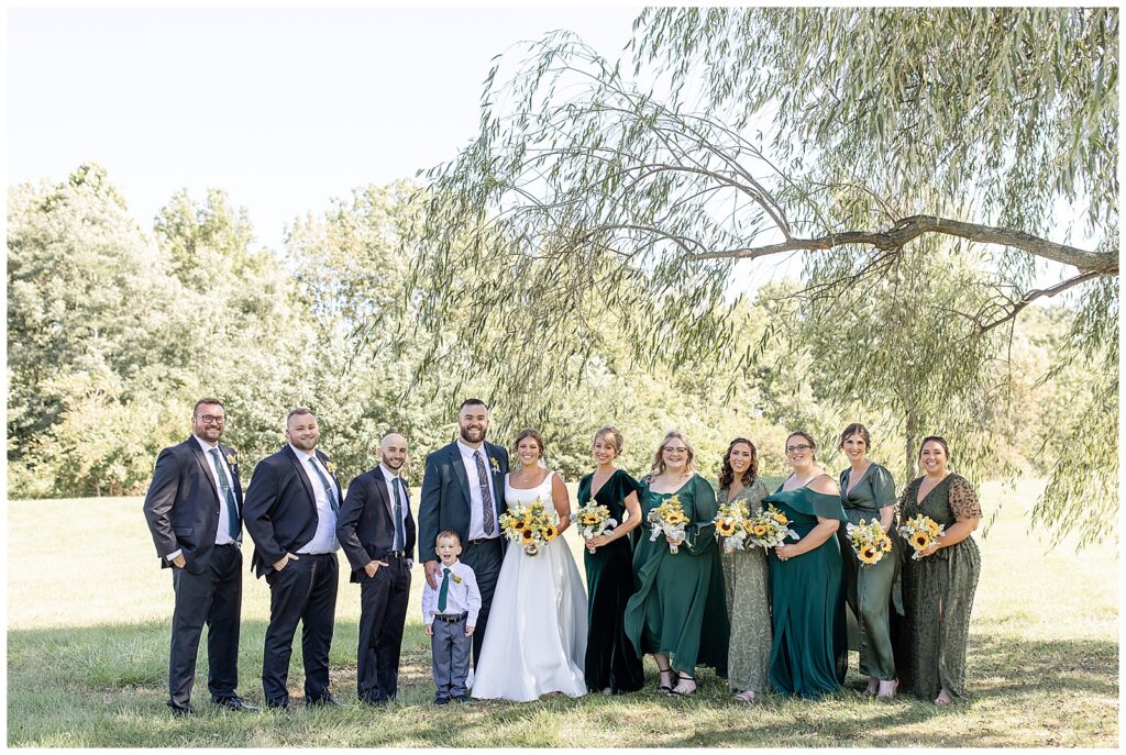 couple with their bridal party with bridesmaids in shades of green gowns and groomsmen in dark suits outside at brick gables