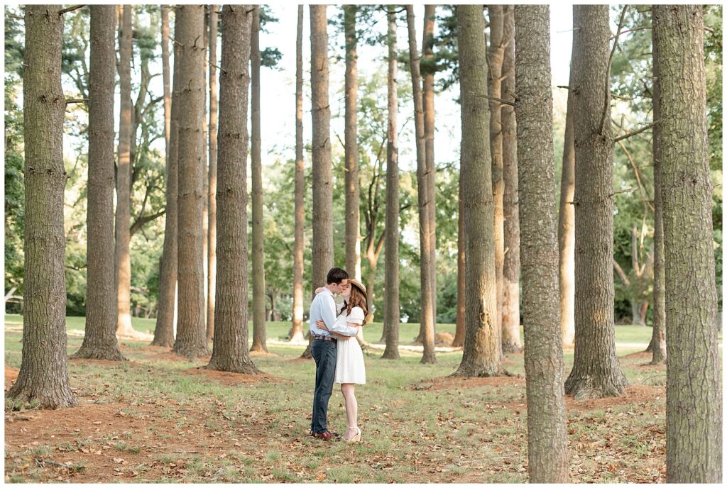 engaged couple kissing and hugging tightly among forest of evergreen trees at sunset at valley garden park