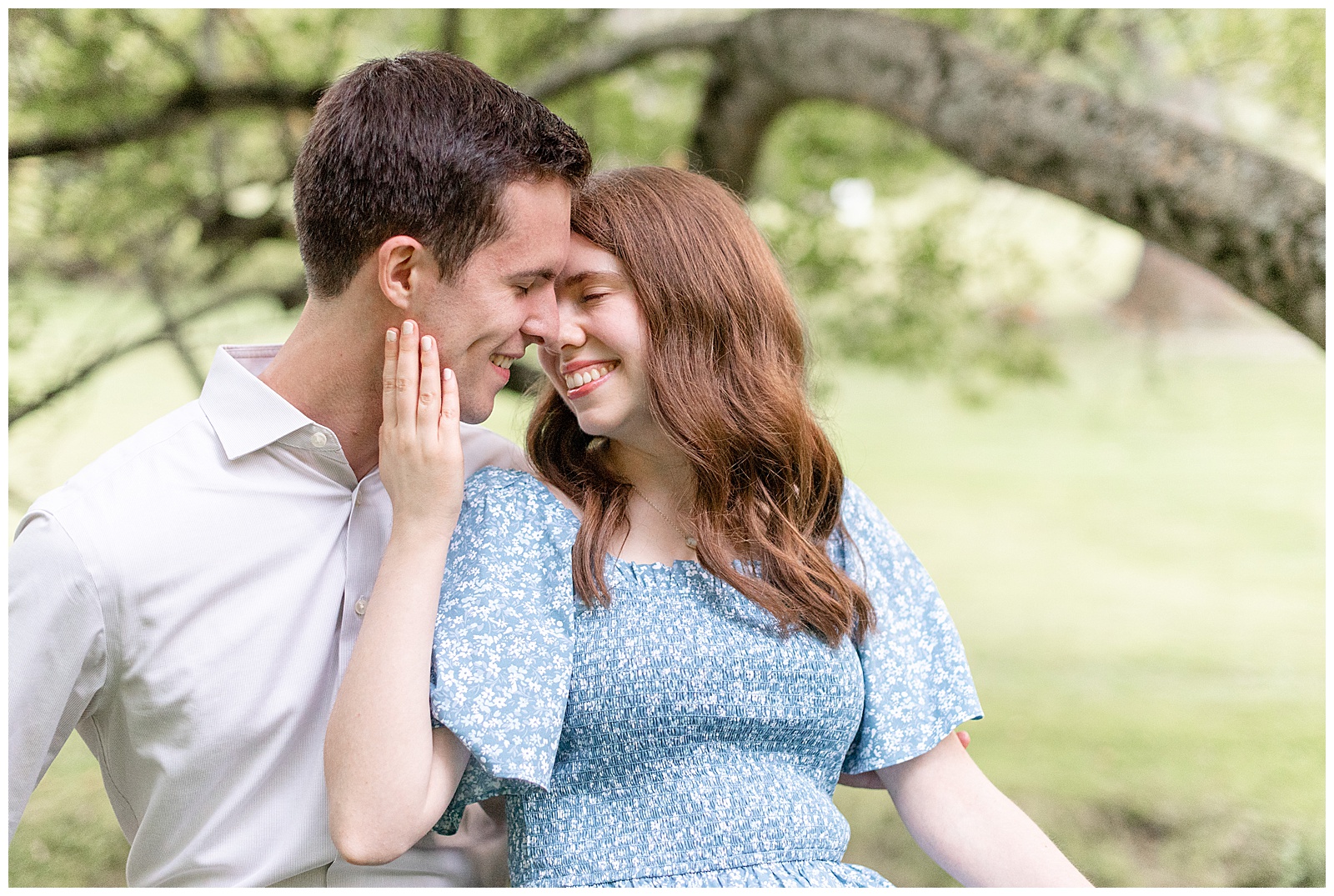 engaged couple almost kissing as girl leans back against guy and gently touches his right cheek with her right hand in delaware park