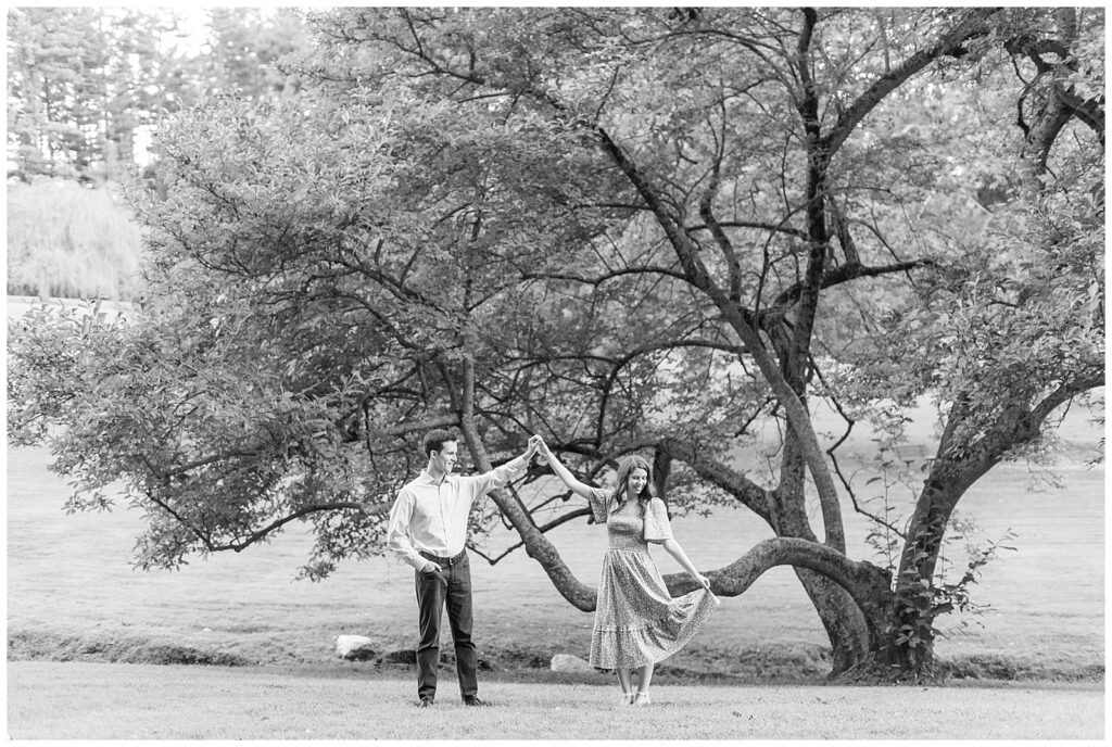 black and white photo of guy twirling girl under his left hand by beautiful tree at valley garden park in delaware