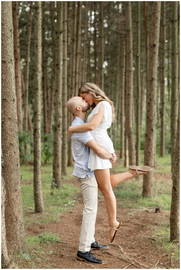 guy lifting girl off the ground as they kiss among rows of evergreens at manheim township park