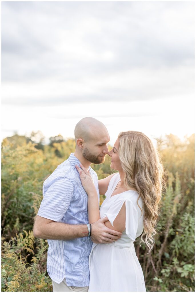 engaged couple almost kissing and standing close in tall wildflower field at sunset at overlook park