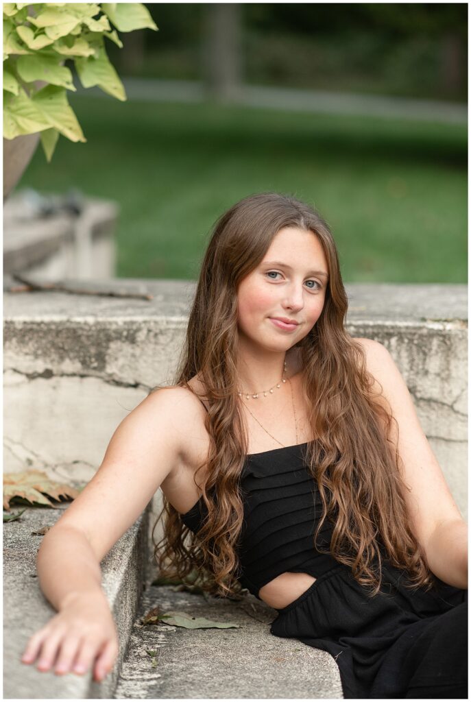 senior girl sitting on concrete step and smirking at camera at hibernia park in pennsylvania