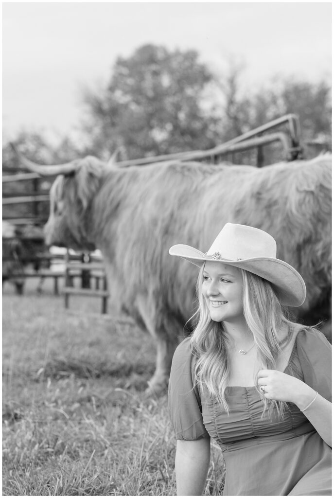 black and white photo of senior girl sitting by highland cow and looking into distance in york pennsylvania
