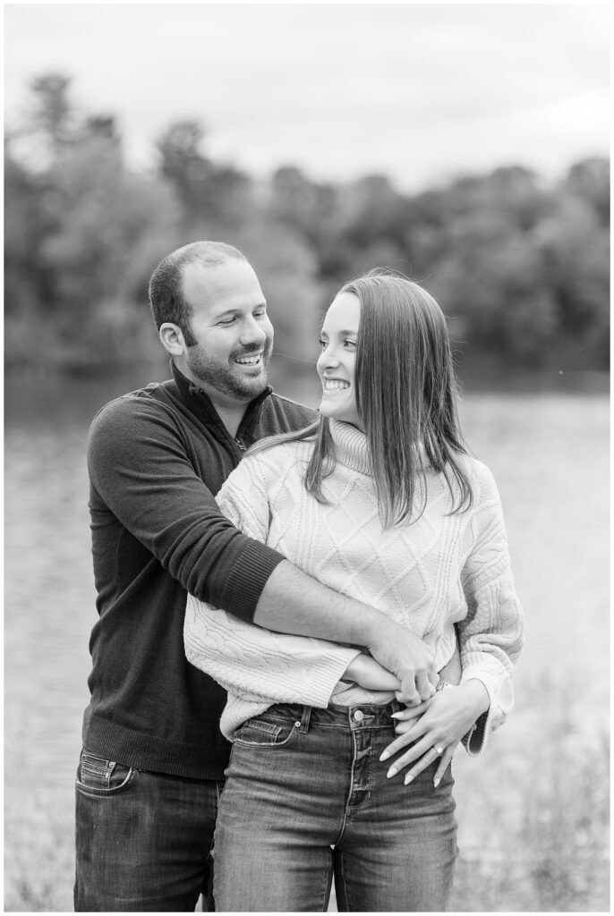black and white photo of guy hugging girl from behind as she looks back and they smile at lake redman