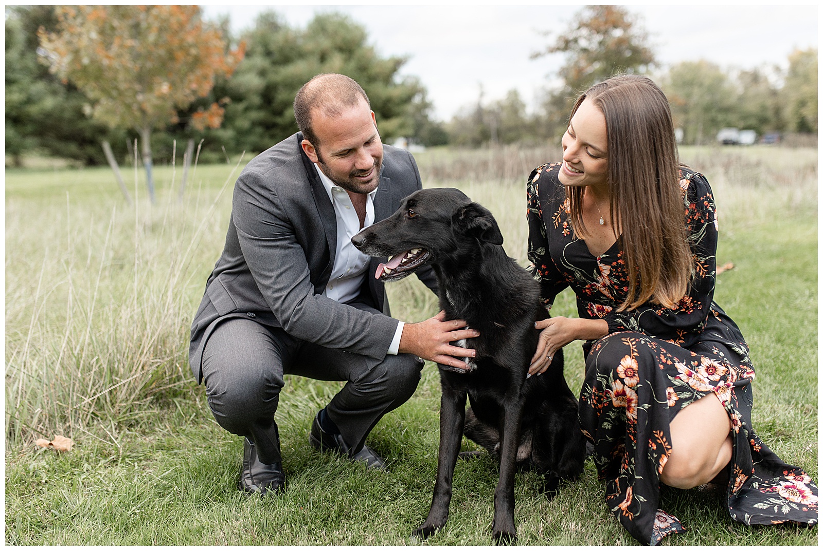 couple crouched down petting their black dog by wild grasses at lake redman