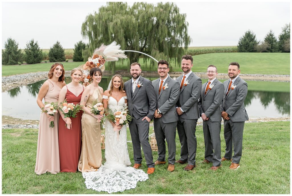 couple with their bridal party standing in front of floral boho archway at lakefield weddings in lancaster county