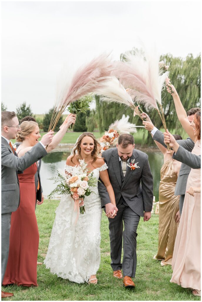 bridal party creating an aisle and holding pink pampas grasses overhead as bride and groom walk through at lakefield weddings