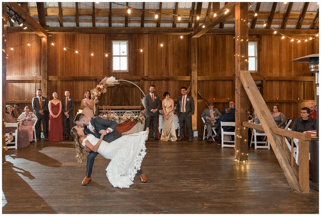 groom dipping back his bride and kissing her during their first dance inside barn reception at lakefield weddings