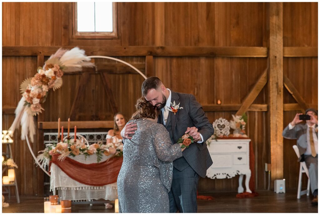 groom dancing with his mom as she rests her right cheek on his chest inside barn at lakefield weddings