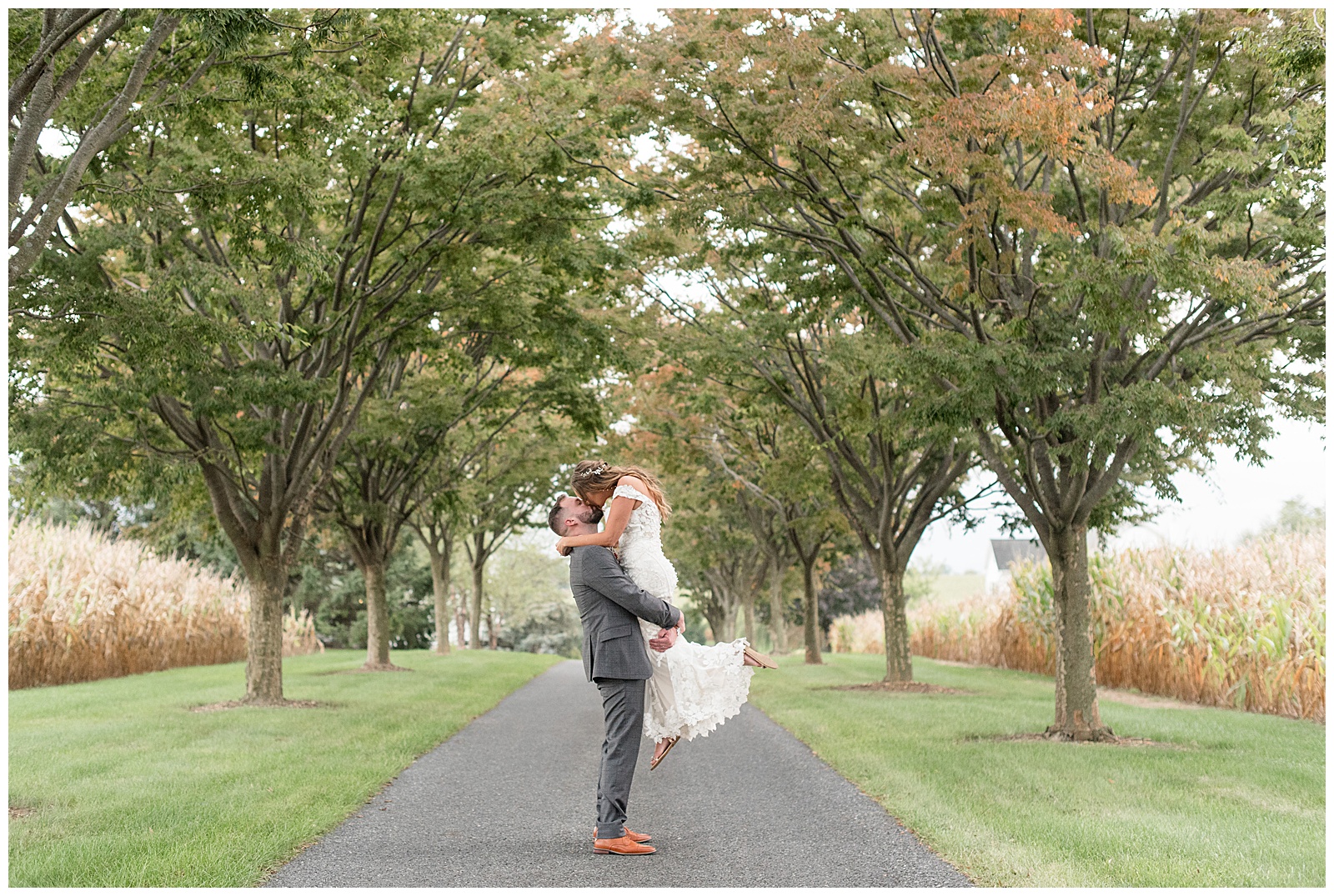 groom lifting his bride off the ground and kissing her on tree-lined pathway at lakefield weddings in lancaster pa