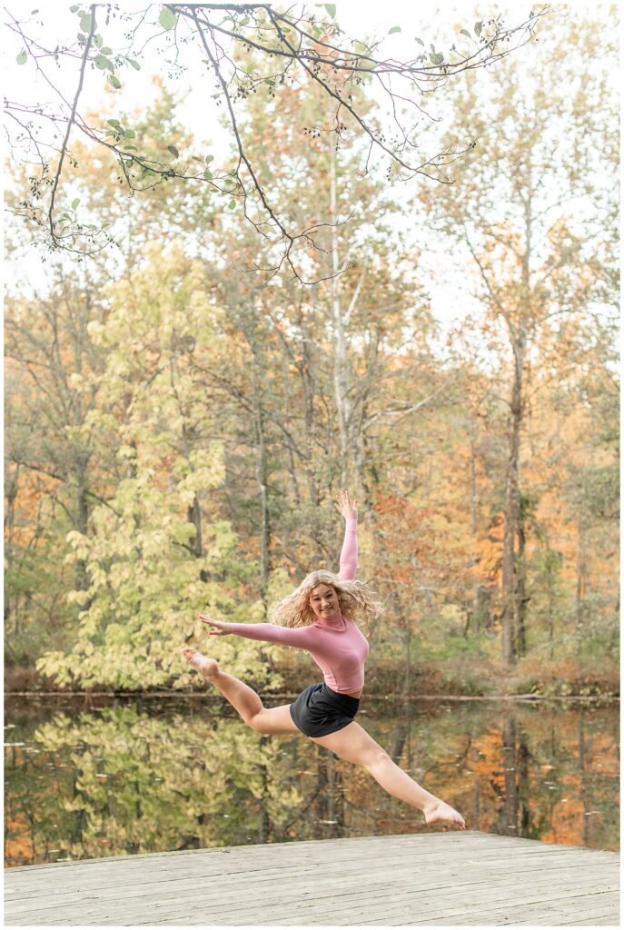 senior girl doing grand jete leap on wooden dock at nolde forest in pennsylvania