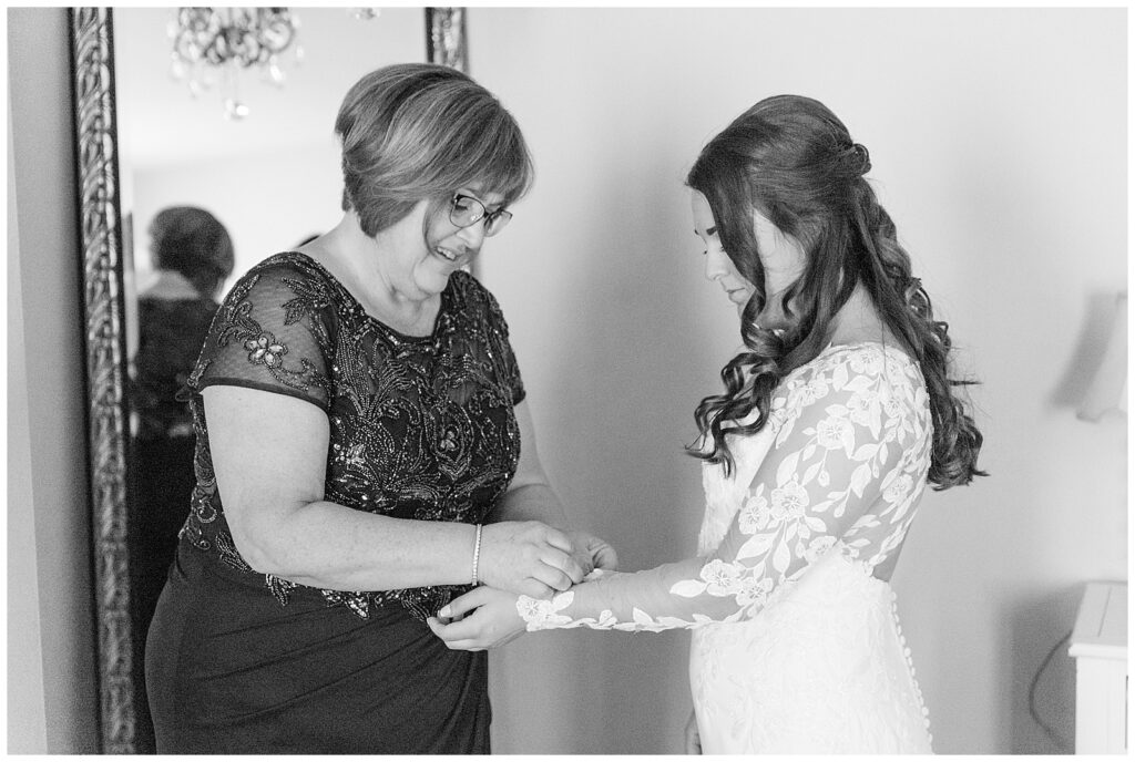 black and white photo of bride's mom helping bride with sleeve of her lacy white wedding gown in montgomery county pennsylvania