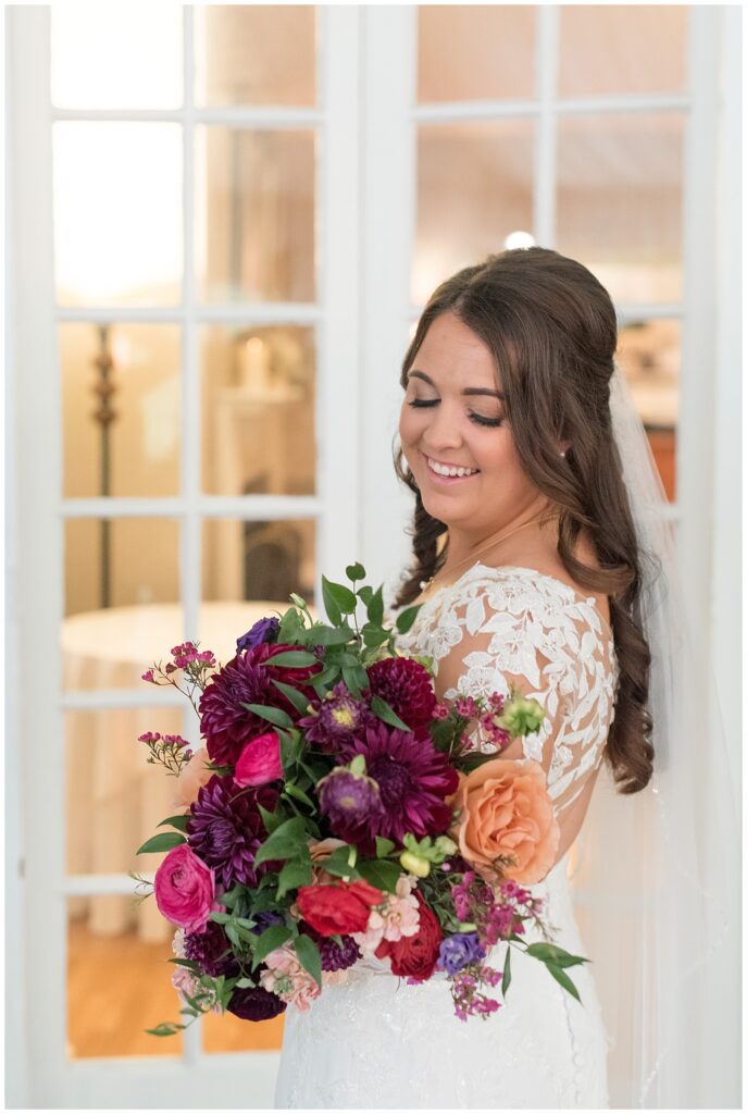 bride holding colorful fall bouquet and looking down and smiling at it at the manor house at prophecy creek