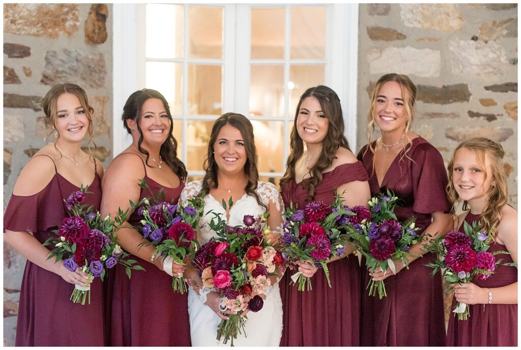 bride with her five bridesmaids all in burgundy gowns standing beside her and all holding bouquets in ambler pennsylvania