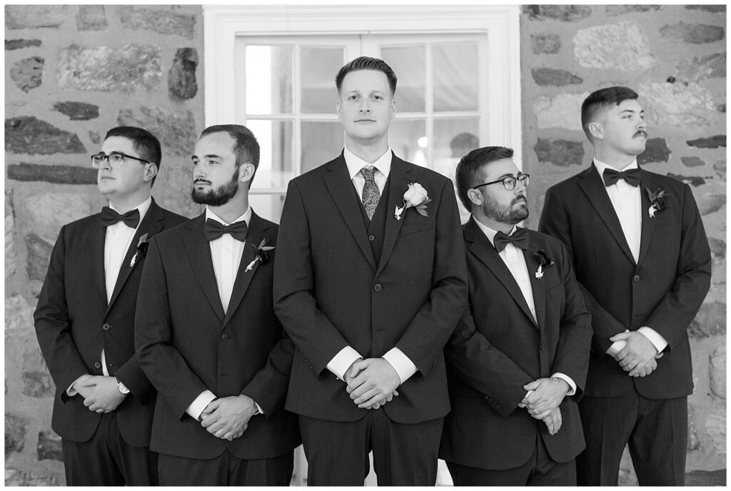 black and white photo of groom standing with his four groomsmen who are looking in opposite directions as groom looks directly at camera in ambler pennsylvania