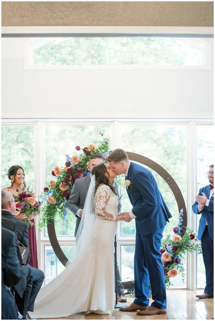couple sharing their first kiss by round wooden floral display indoors at the manor house at prophecy creek