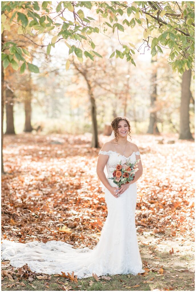 bride in leaf-covered forest with the sun peeking through the trees holding colorful bouquet at lauxmont farms
