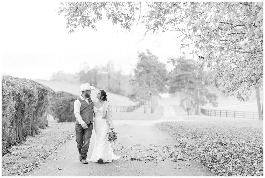 black and white photo of couple side hugging as they walk towards camera along lane at lauxmont farms