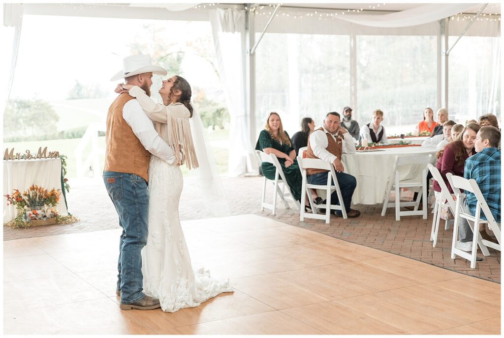 couple sharing their first dance on dance floor under white tent as guests watch at lauxmont farms in york pennsylvania