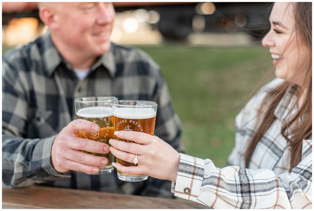 couple tapping their glasses of beer together as they sit at picnic table at bespoke brewery in strasburg pennsylvania