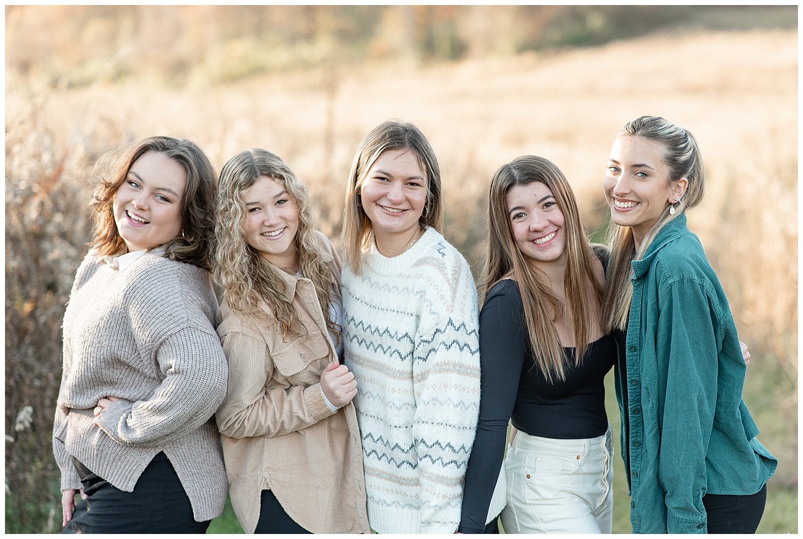 five senior girls huddled together and smiling with wild grass field behind them at middle creek wildlife management area
