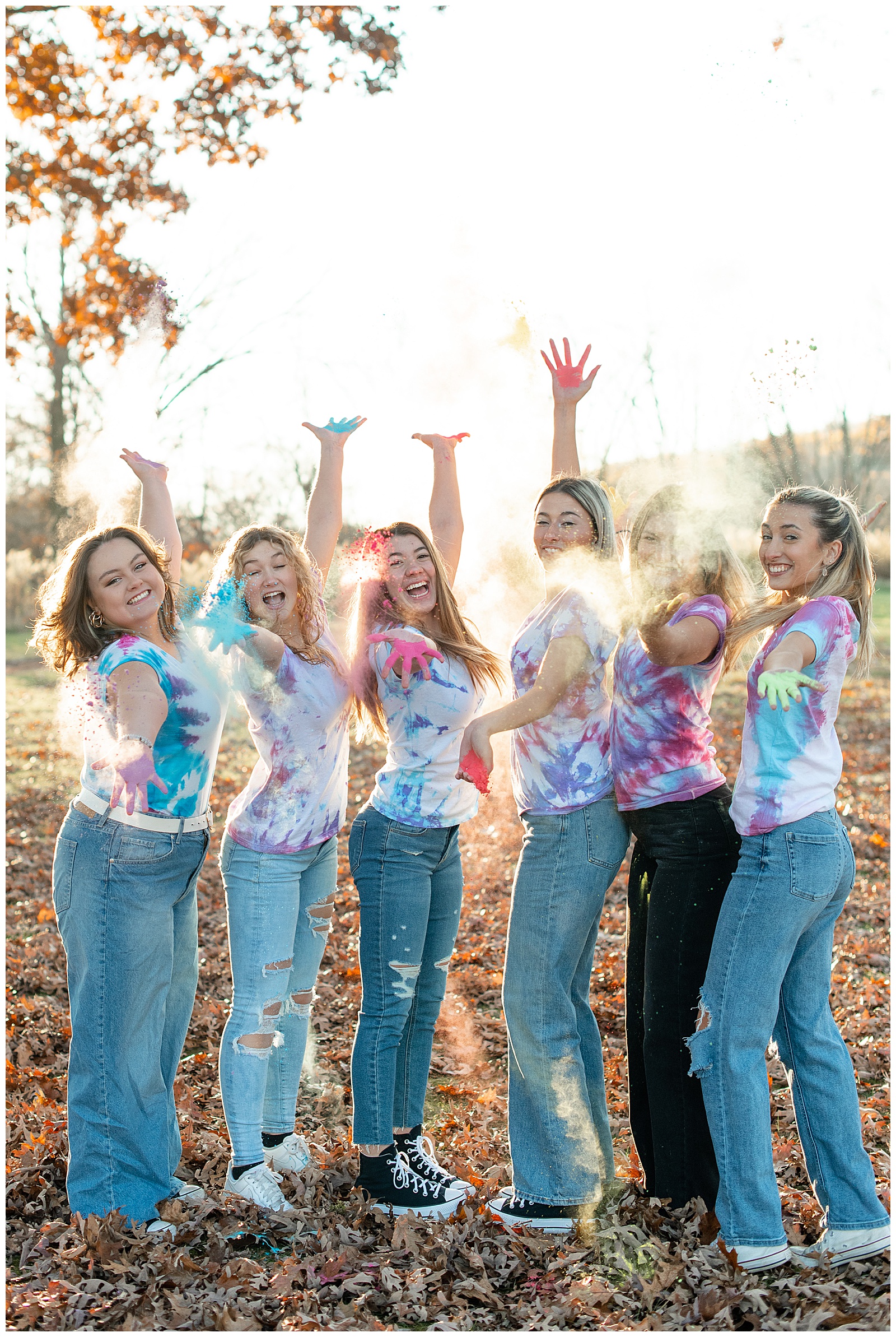 senior girls in tie dye shirts and jeans throwing colored powder towards camera at middle creek