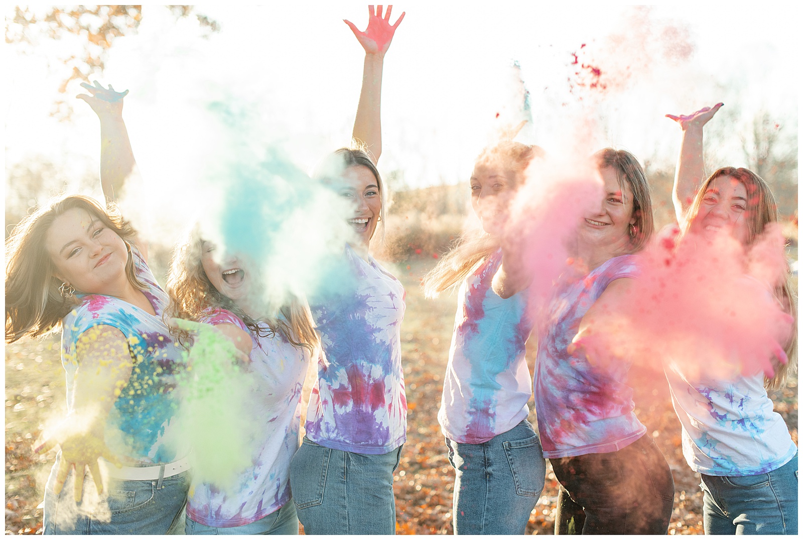 senior girls behind a cloud of colorful powder with arms extended at sunset at middle creek wildlife management area