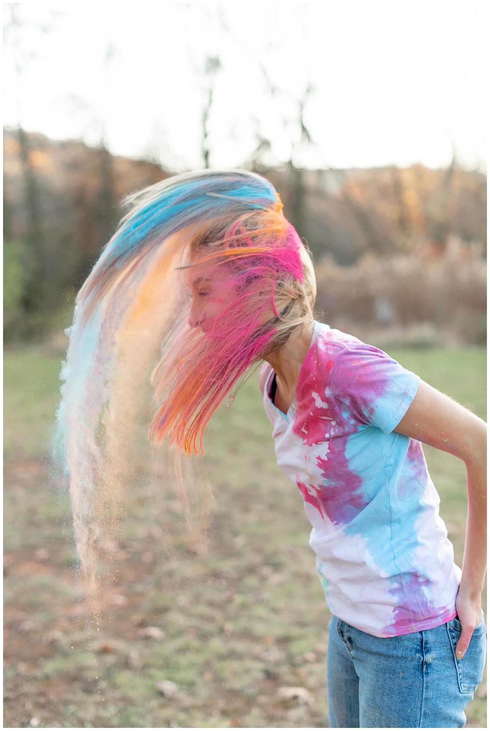 senior girl with pink, orange, and blue colored hair flinging her hair back and powder flying at middle creek