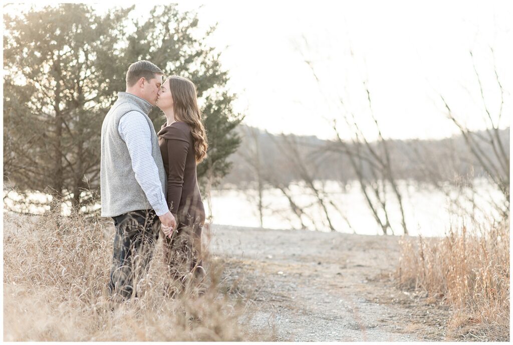engaged couple kissing by dried wild grasses with river in background at white cliffs of conoy in lancaster county