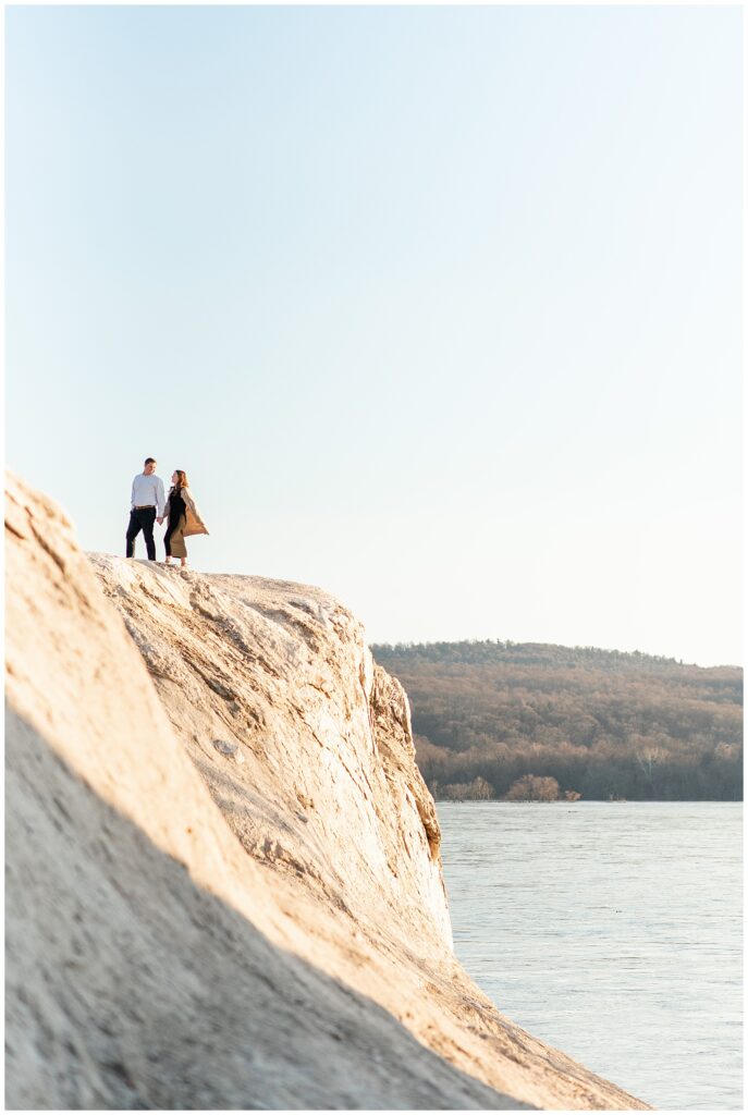 engaged couple atop the white cliffs of conoy on sunny winter day with the susquehanna river below them