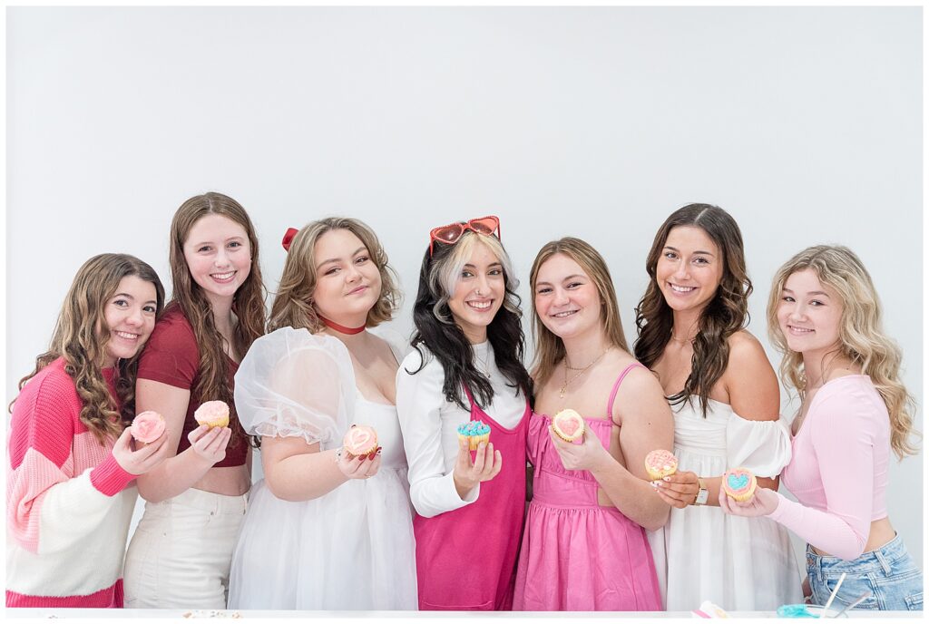 seven female senior spokesmodels in shades of pink and white holding cupcakes at haven studios